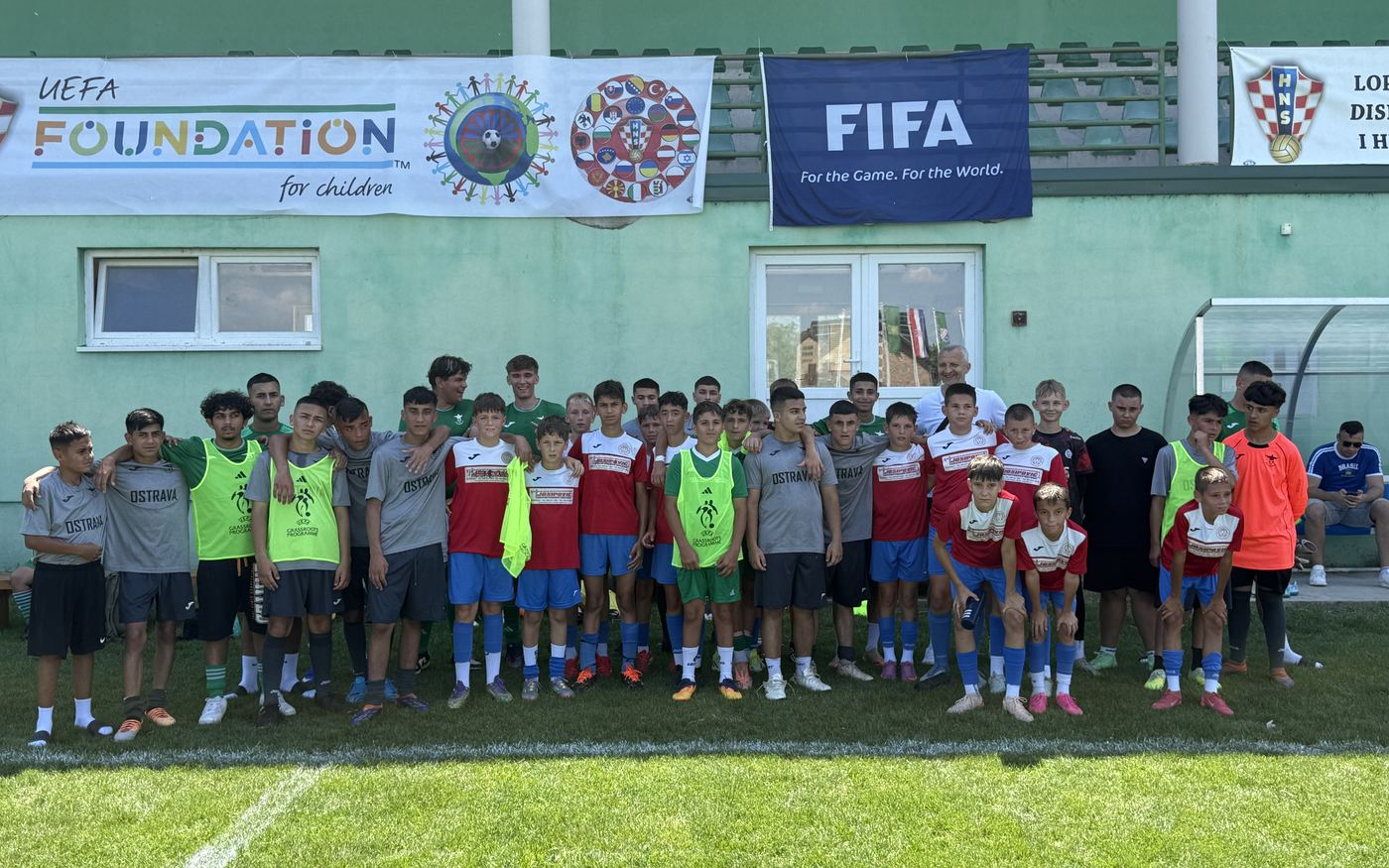 Hráči a trenéři na mezinárodním turnaji před budovou s logy UEFA Foundation a FIFA
