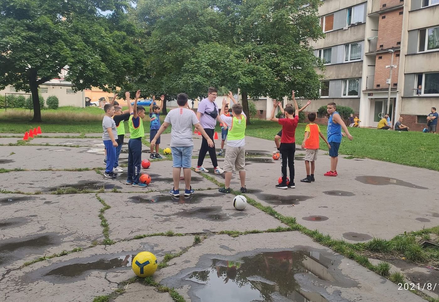 Rozbitý betonový plácek, na kterém si hrají děti se sídlištěm v pozadí