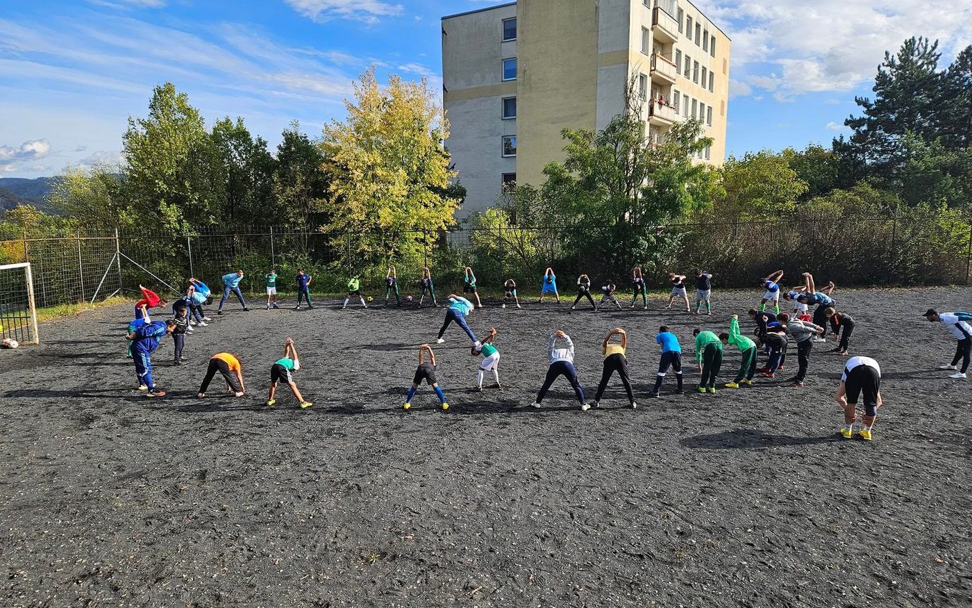 Děti se rozcvičují na štěrkovém hřišti u paneláku